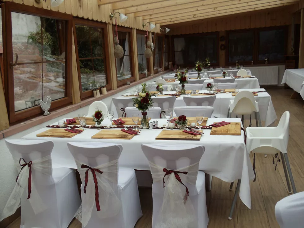 Festlich gedeckte Tische im Hilsighof Festlich gedeckte Tische mit weißen Hussen und roten Schleifen in einem Raum mit großen Fenstern.